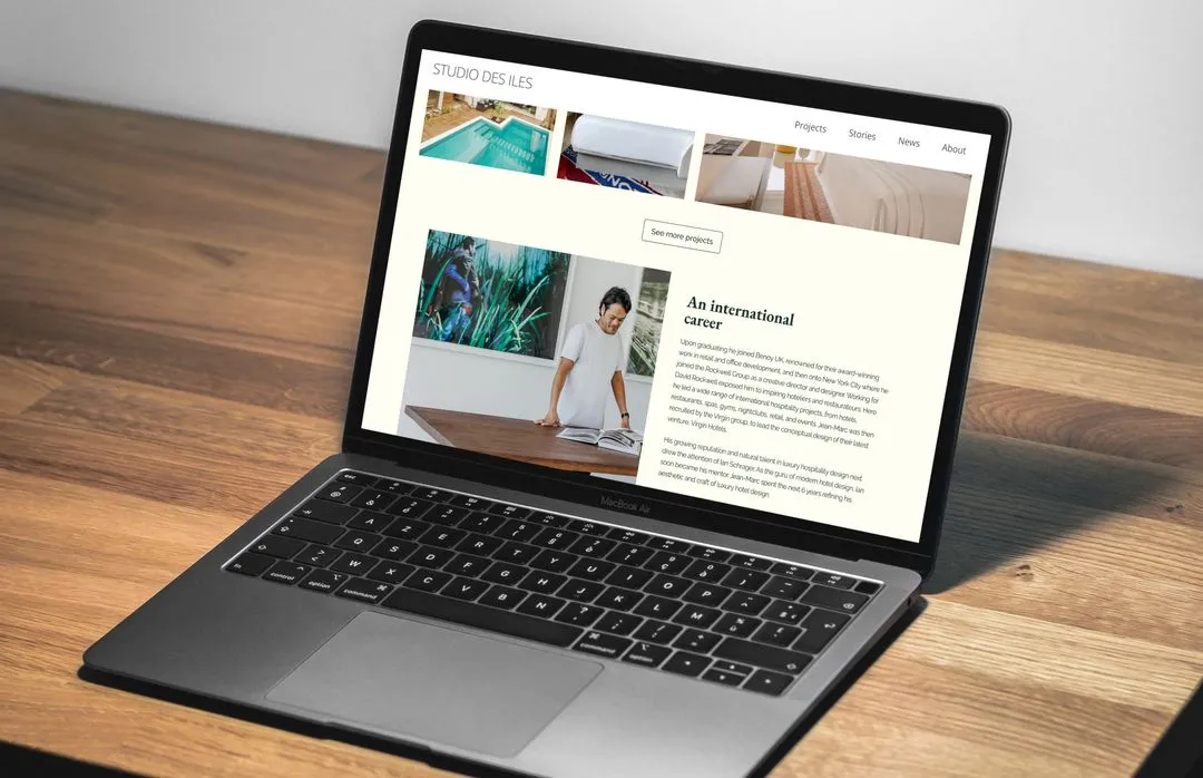 Open laptop on wooden table displaying STUDIO DES ILES website featuring an article titled 'An international career' with a photo of a man in a white t-shirt.